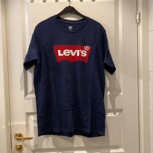Blå t-shirt från Levi's - Säljer en snygg blå t-shirt från Levi's i storlek L. Den har en klassisk röd och vit logga på bröstet. 
