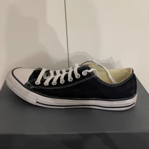 Svarta Converse All Star sneakers - Klassiska svarta Converse All Star sneakers i canvas med vit sula och snörning. Perfekta för vardagsbruk och ger en avslappnad stil. De har den ikoniska loggan på hälen och är i bra skick.