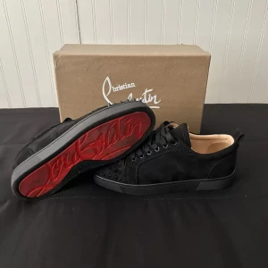Svarta Christian Louboutin - Säljer ett par svarta sneakers från Christian Louboutin i nyskick. De har en cool design med nitar på tån, samt den ikoniska röda sulan. Skorna är i skinn och mocka med snörning. Perfekta för att ge din outfit en edgy touch! Skick: 10/10 