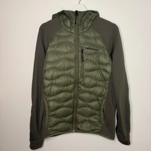 Grön jacka från Peak Performance - Säljer en snygg grön jacka från Peak Performance i storlek M och i mycket fint skick. Jackan har en quiltad design med dragkedja och huva, perfekt för kyliga dagar. Den är långärmad och har en stilren look som passar både till vardags och utomhusaktiviteter. Den är i storlek M men passar S. 