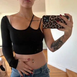 Svart oneshoulder topp - Säljer en svart oneshoulder topp som är supertrendig och perfekt för fest. Den är croppad och har en lång ärm på ena sidan medan den andra är ärmlös. Materialet är stretchigt och bekvämt, vilket gör den idealisk för en utekväll. Passar perfekt med jeans eller kjol!