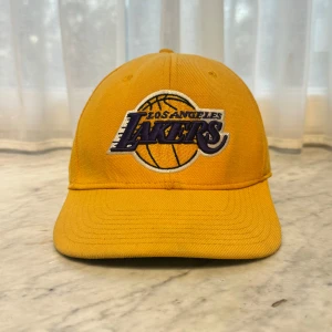Gul Los Angeles Lakers keps från Mitchell & Ness - Säljer en gul keps med Los Angeles Lakers logga, perfekt för alla basketfans! Kepsen är från Mitchell & Ness och har en broderad logga på framsidan. Den är en del av NBA Hardwood Classics-kollektionen.    🧢 Jag har flera kepsar till salu på min profil och lägger upp nya modeller regelbundet. 