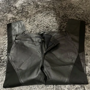 Svarta byxor från Zay - Snygga svarta byxor från Zay i skinnimitation. De har en tight passform och dragkedja fram. Perfekta för en cool och stilren look. Passar bra till både vardag och fest!