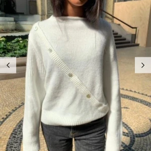 Vit stickad tröja med knappar - Säljer en stilren vit stickad tröja med unika diagonala knappar över framsidan. Tröjan har långa ärmar och en rund halsringning, perfekt för kyligare dagar. Passar bra till både jeans och kjol.