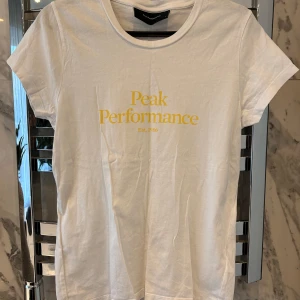 Vit t-shirt från Peak Performance - Säljer en  vit t-shirt från Peak Performance med gul text på framsidan. Storlek S, köparen står för frakten! 💗