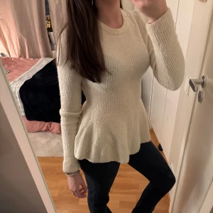 Beige ribbad tröja - Säljer en stilren beige ribbad tröja med lång ärm och volangdetalj vid nederkanten. Perfekt för en chic och bekväm look. Passar bra till jeans eller kjol.