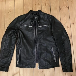 Svart skinnjacka med dragkedjor - Snygg svart skinnjacka från Crocker®️ i storlek M. Jackan har flera dragkedjor och en stilren design med långa ärmar. Perfekt för en cool look. Aldrig använd, fick den i present men passade inte mig. Dm mig för fler bilder! Pris kan diskuteras.