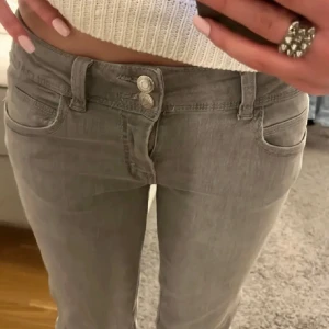 Grå jeans med låg midja - Snygga grå jeans med låg midja och en tight bootcut passform. De har klassisk femficksdesign och stängs med dragkedja och knapp. Perfekta för en stilren look.