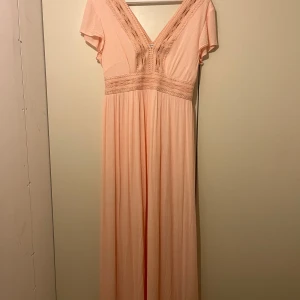 Klänning - Elegant ljusrosa långklänning från Bodyflirt med v-ringning och spetsdetaljer. Använd en gång. 