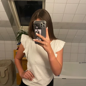 Vit topp från H&M - Säljer en söt vit topp från H&M med volangdetaljer på ärmarna. Toppen är i ett mjukt bomullsmaterial och har en rund halsringning. Perfekt för sommaren. Aldrig använt 