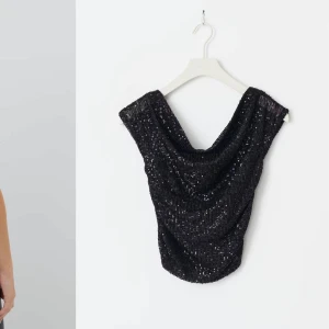Svart glittrig offshoulder topp - Snygg svart glittrig offshoulder topp med paljetter. Perfekt för en kväll ute. Toppen har en lös passform och ärmlös design med en elegant drapering.
