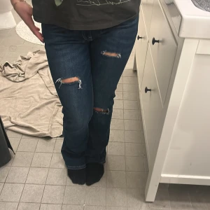 Blå jeans från Gina Tricot - Snygga blå jeans från Gina Tricot med slitna detaljer på knäna. Midjemåttet är 38cm rakt över och innerbenslängden ca 78. Köpta för ca 500kr