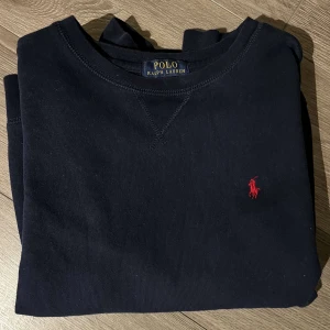 Svart hoodie Ralph Lauren - Säljer en stilren svart hoodie från Polo Ralph Lauren med det klassiska röda logotypen på bröstet. Hoodien har långa ärmar och en rund halsringning. Perfekt för en avslappnad och snygg look.