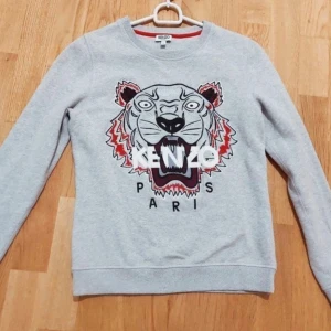 Kenzo - Säljer en grå sweatshirt från Kenzo med ett stort tigertryck och texten 'Kenzo Paris' på framsidan. Tröjan har långa ärmar och en rund halsringning. Perfekt för en stilren och trendig look.