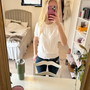 Vit kortärmad tröja - Säljer en stilren vit tröja med korta ärmar. Tröjan har en rund halsringning och ribbade kanter vid ärmslut och nederkant.