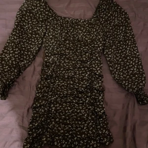 Brun blommig klänning från Shein - Säljer en söt brun klänning från Shein med små vita blommor. Klänningen har långa ärmar och en smickrande rynkad design. Perfekt för en stilfull look!