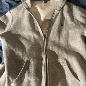 Grå Ralph lauren zip hoodie - Nu säljer jag en stilren Ralph lauren zip hoodie i färgen grå. Den är i ett väldigt bra skick bara använt den ett fåtal gånger. Den är köpt för 1199kr så hos mig får ni den för 499kr ett riktigt bra pris för en dunder tröja.