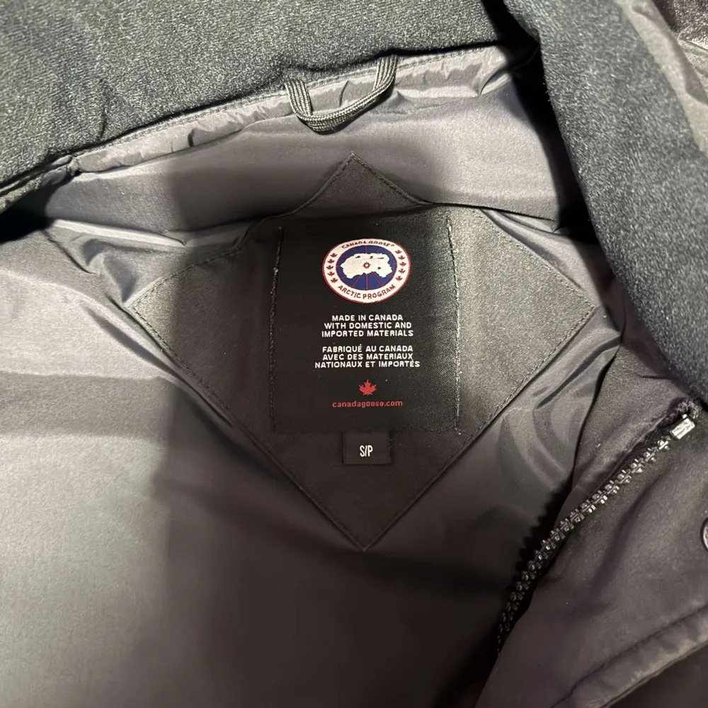 Säljer en svart dunväst från Canada Goose med dragkedja och knappar. Västen har en broderad logotyp på bröstet och praktiska fickor framtill. Perfekt för kyligare dagar. Ser bättre ut i verkligheten (Äkta)!!!. Takit.