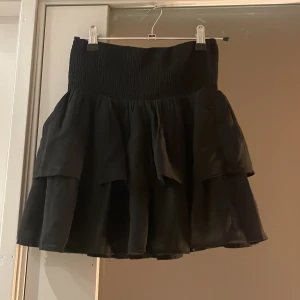 Svart kjol från KappAhl - Snygg svart kjol från KappAhl med volangdetaljer. Kjolen har en elastisk midja för bekväm passform och en flerdelad design som ger en fin volym. 