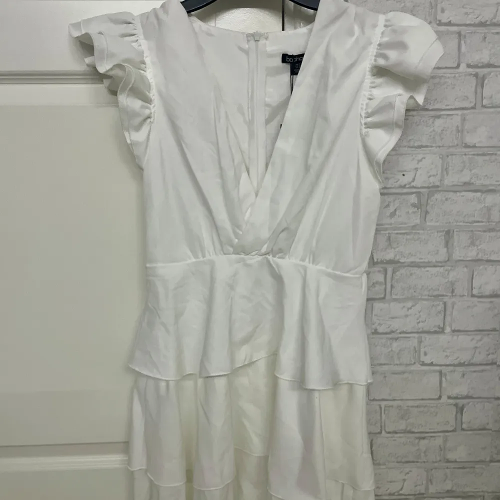 Ny söt vit klänning från Boohoo med volanger och v-ringning. Klänningen är aldrig använd, har korta ärmar och en fin volangdetalj i midjan som ger en lekfull look. Perfekt till midsommar, student eller utomlandsresor🌸. Mekot.