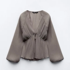 Grå blus från Zara - Säljer en elegant grå blus från Zara med långa ärmar och knytning framtill. Blusen har en plisserad design som ger en stilren look. Perfekt för att lyfta vilken outfit som helst. Nyskick