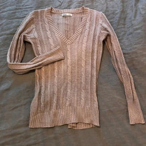 Beige stickad tröja från Old Navy - Säljer en beige stickad tröja från Old Navy med v-ringning och kabelstickat mönster. Tröjan har långa ärmar och ribbade kanter vid ärmslut och nederkant. Perfekt för kyligare dagar!