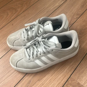 Grå sneakers från Adidas - Snygga grå sneakers från Adidas i mocka med klassiska vita ränder på sidan. Skorna har snörning. Köpta för ca 1 år sen i stadium butik.!!!Äkta!!! 