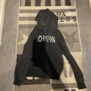 Svart hoodie från Jordan - Säljer en svart hoodie från Jordan med stor logga på framsidan och nummer 23 med grafiskt mönster på baksidan. Hoodien har en rymlig ficka framtill och justerbar huva. Perfekt för en sportig look!