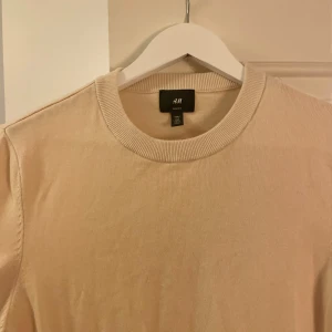 Beige tröja - Säljer en stilren beige tröja från H&M. Tröjan har en rund halsringning och ribbade muddar vid ärmslut och nederkant. Perfekt för en avslappnad look.