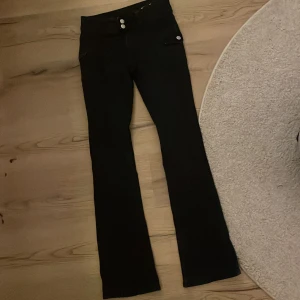 Svarta jeans med sido fickor - Snygga svarta jeans med bootcut-stil och low waist som det står. Byxorna har dekorativa knappar och två fickor på sidorna fram. Perfekta för en stilren look. Storlek 170