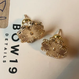 Guld örhängen blomma - Söta örhängen i mässing med 18 karat guld överdrag. Ser ut lite som en blomma eller lycko klöver och riktigt fina. Fick flera liknande varandra i julklapp så säljer de ena paret då jag använt de andra. Helt nya och oanvända alltså. Lite större modell på stud örhänge helt allergi säkra 