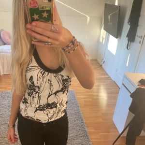 Svartvit mönstrad linnetopp - Säljer en snygg svartvit linnetopp med ett abstrakt blommönster. Toppen har en rund halsringning med svarta kanter och är ärmlös. Perfekt för en stilren look. På bilden har jag knutit en toft för att tröjan ska bli mer figursydd