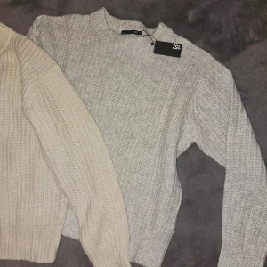 Stickade tröjor  - Två stickade tröjor i beige och grått. Perfekta för kyligare dagar med sin mysiga och varma känsla. Tröjorna har en klassisk design med rund hals och långa ärmar.
