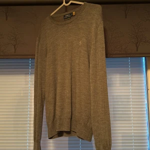 Grå tröja från Polo Ralph Lauren - Säljer en stilren grå tröja från Polo Ralph Lauren i merinoull. Tröjan har en diskret broderad logga på bröstet och rund halsringning. Perfekt för en klassisk och bekväm look. Priset kan diskuteras! Hör av er vid minsta fråga!