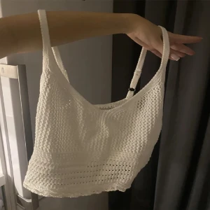 Vit stickad croppad topp - Säljer en superfin vit stickad croppad topp. Den är ärmlös med smala axelband och har en snygg, luftig stickning som passar perfekt till sommaren. Toppen är både bekväm och stilren, perfekt för en dag på stranden eller en somrig fest.