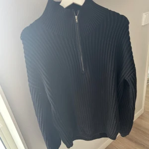 Svart ribbad tröja med dragkedja - Säljer en svart ribbad tröja med dragkedja i halsen. Den är supermysig och perfekt för höst och vinter. Tröjan har långa ärmar och en normal passform. Perfekt för att hålla sig varm och stilren!