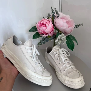 Vita Converse All Star sneakers - Säljer ett par klassiska vita Converse All Star sneakers. De har en tidlös design med snörning och är tillverkade i slitstarkt material. Perfekta för vardagsbruk och passar till nästan alla outfits. Skorna är i bra skick och redo för en ny ägare!