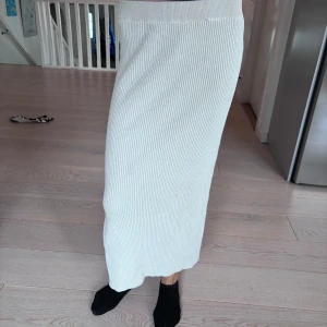 Vit ribbad långkjol - Säljer en superfin vit ribbad långkjol som är perfekt för både vardag och fest. Kjolen har en stilren design med en liten slits på sidan som ger en snygg detalj. Den är gjord i ett mjukt och stretchigt material som sitter bekvämt hela dagen. Passar perfekt till en stickad tröja eller en enkel topp. 🖤