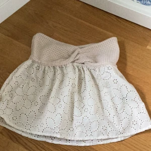 Söt topp med spetsdetaljer - Den här kjolen är supergullig med en beige stickad midja som har en twistdetalj framtill. Den är vit med ett vackert blommigt spetsmönster som ger en romantisk känsla. Perfekt för sommarens alla fester eller en mysig vårdag. från Shein. Aldrig använ!