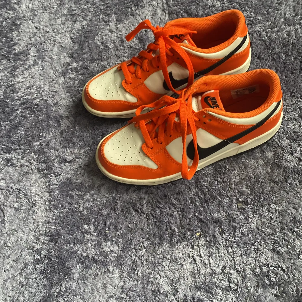 Säljer ett par snygga Nike sneakers i en cool orange och vit färgkombination. Skorna har en klassisk design med snörning och en svart Nike-logga på sidan. Perfekta för både vardag och träning!. Skor.