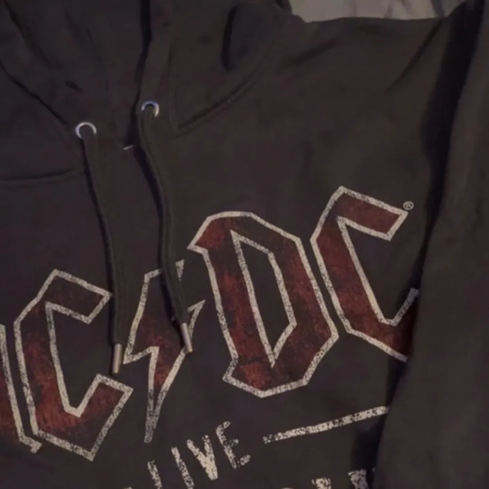 Säljer en svart AC/DC hoodie från H&M. Den har ett coolt tryck med 'AC/DC Live World Tour' i rött och vitt på framsidan. Perfekt för rockälskare! Den är i storlek L och har en skön passform med långa ärmar och dragsko i huvan.. Tröjor & Koftor.