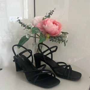 Svarta sandaler med klack från Alley - Säljer ett par eleganta svarta sandaler med klack från Alley. De har en stilren design med smala remmar och en liten spänne vid ankeln. Perfekta för sommarens fester eller en utekväll. Använda men i bra skick!