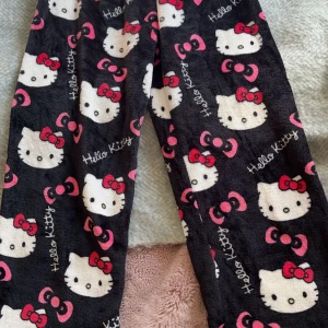 Hello Kitty mjukisbyxor - Supermysiga Hello Kitty mjukisbyxor i svart med ett gulligt mönster av Hello Kittys ansikte och rosa rosetter. Perfekta för att chilla hemma eller ha en avslappnad dag. De är gjorda i ett mjukt och skönt material som känns härligt mot huden. (de vita på sista bilden finns i en annan annons)🩷
