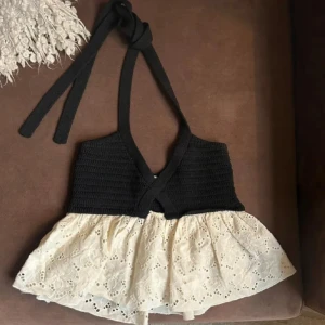 Svart och vit topp med spetsdetaljer - Säljer en superfin svart och vit topp med spetsdetaljer. Den har en stickad överdel och en vacker spetskant nedtill. Perfekt för sommardagar eller en festlig kväll. Toppen har en knytning i nacken och en liten öppning framtill. Passar perfekt till jeans eller kjol!