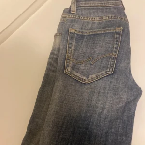 Blå jeans från Jack & Jones - Säljer ett par snygga blå jeans från Jack & Jones i bra skick. De har en klassisk femficksdesign och är tillverkade i slitstarkt denim. Perfekta för både vardag och fest! Passar bra till en casual look eller med en skjorta för en mer uppklädd stil.