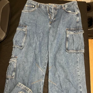Blå cargopants i jeansmaterial - Säljer ett par blå cargopants i jeansmaterial. De har flera praktiska fickor på sidorna och en loose passform. De är mif Waits och väldigt baggy. De har även snygga detaljer vid foten. Tycker dessa är skitsnygga på men dem är för stora på mig.