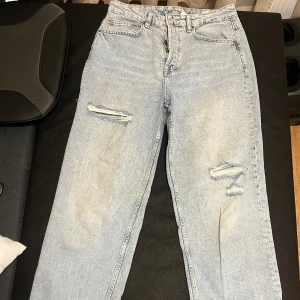 Ljusa jeans med slitningar - Säljer ett par ljusa jeans med slitningar på låren. De har en avslappnad passform och är perfekta för en casual look. De är också high waisted. 