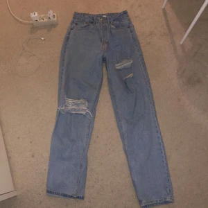 Blå jeans med slitningar - Säljer ett par blå jeans med coola slitningar på låren. De har en klassisk femficksdesign och är perfekta för en avslappnad stil. Passar bra till både sneakers och boots. Perfekt för vardagsbruk eller en chill kväll med vänner.