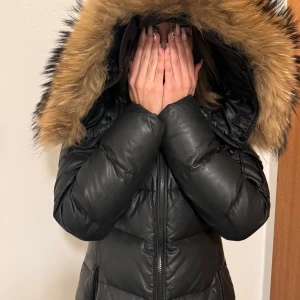 Svart dunjacka med pälskrage - Söker du en elegant o varm jacka inför vinter? Här har du en Hollies jacka med äkta päls. Mycket sparsamt anänd, ej under snö eller regn, vilket gjorde att jackans kvalitet är i mycket fint skick än. Pälsen är som ny. Defekt: 1.Ficka höger - Dragkedjehallare saknas men gar att stänga fickan ända 2. Litet hal i vänstra ficka, gar att sy pa 2 minuter. 3. Saknas ett litet magnet bit pa luvans rep (se sista bild)