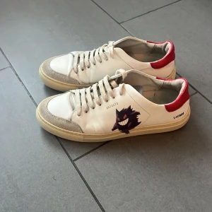 Arigato sneakers stlk 42 - Säljer ett par vita sneakers från Axel Arigato med  Pokemon design på sidan. Skorna har snörning och är i bra skick, väldigt begränsad användning.